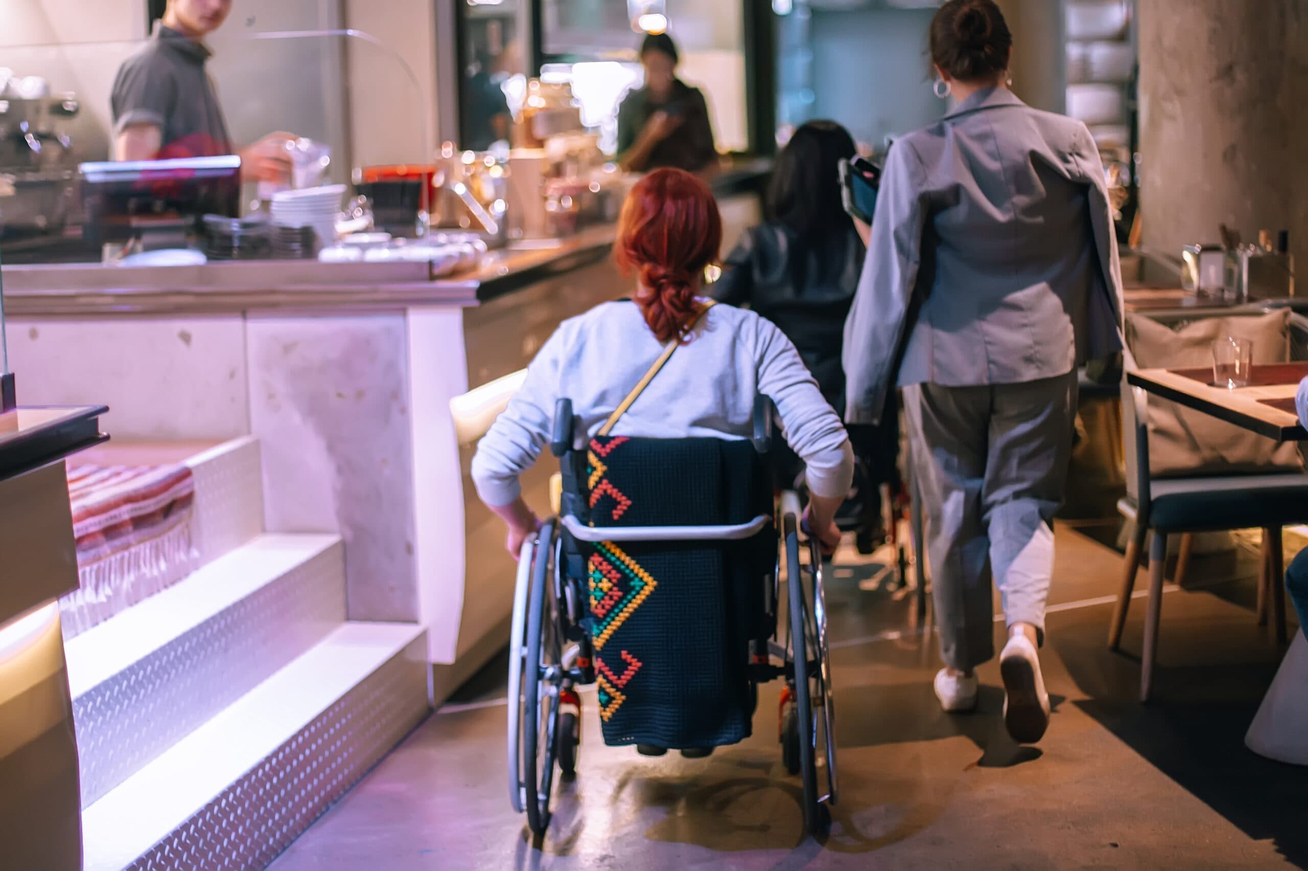 A person in a wheelchair moving through a café with a companion